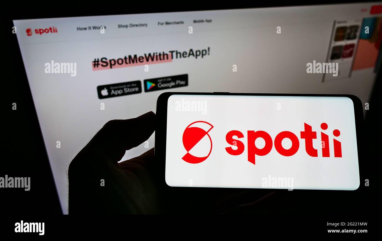 Personne tenant le téléphone portable avec le logo de la plate-forme de paiement de la société Spotii DMCC à l'écran en face de la page Web d'affaires. Mise au point sur l'affichage du téléphone. Banque D'Images