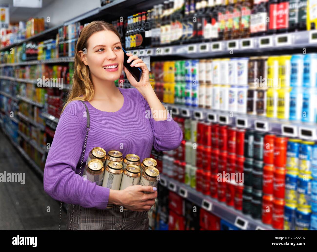 une femme achète de la bière en conserve dans l'hypermarché et parle sur un téléphone mobile Banque D'Images