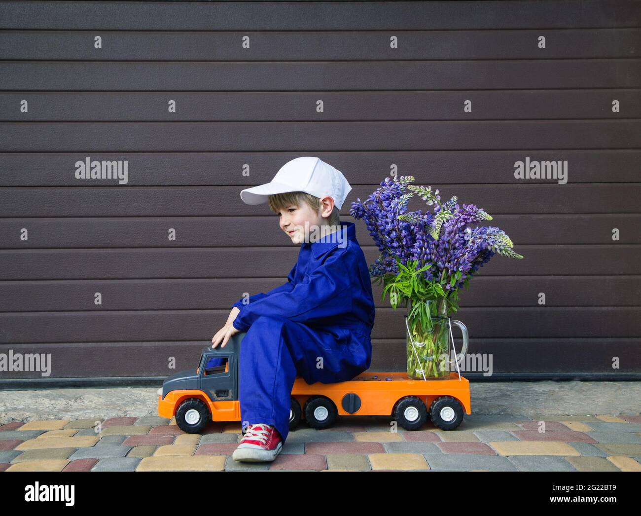 drôle mignon garçon de 4-5 ans dans une combinaison bleue mécanique et une  casquette est assis dans le profil d'un camion de jouet avec un grand  bouquet de fleurs. Concept de livraison,