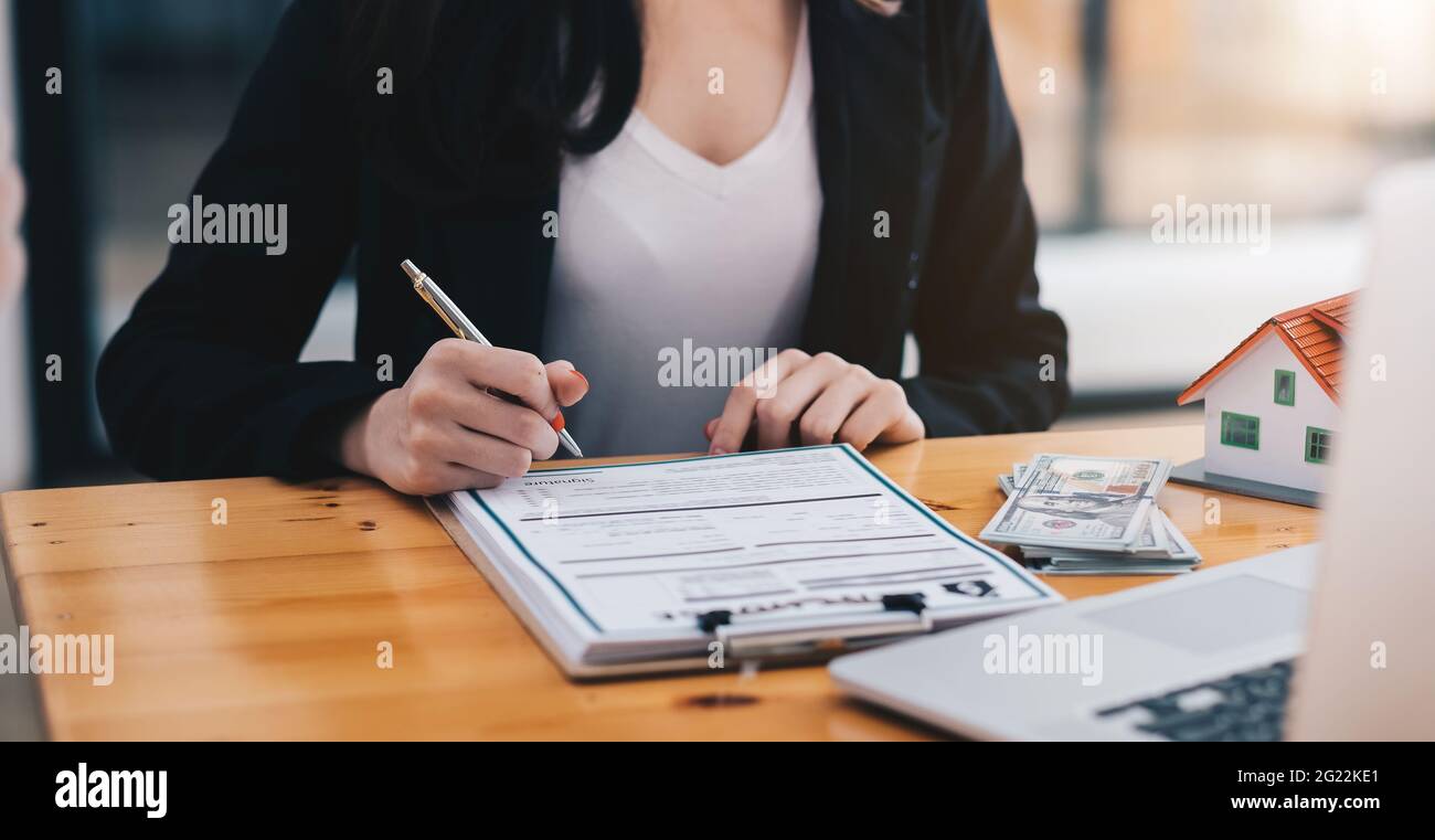 gros plan des mains de femme d'affaires signant le crédit-bail de documents et modèle de maison sur un bureau en bois Banque D'Images