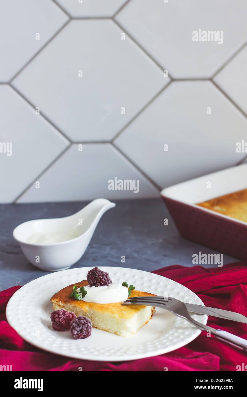 Cocotte de fromage cottage sur une assiette blanche et thé dans une tasse bordeaux sur fond gris Banque D'Images