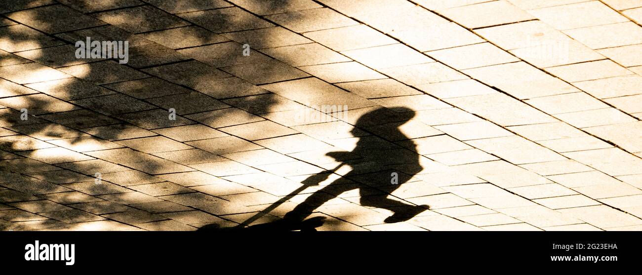 Silhouette d'ombre floue d'un enfant à bord d'un scooter, sous un arbre dans le parc par temps ensoleillé, en sépia noir et blanc Banque D'Images