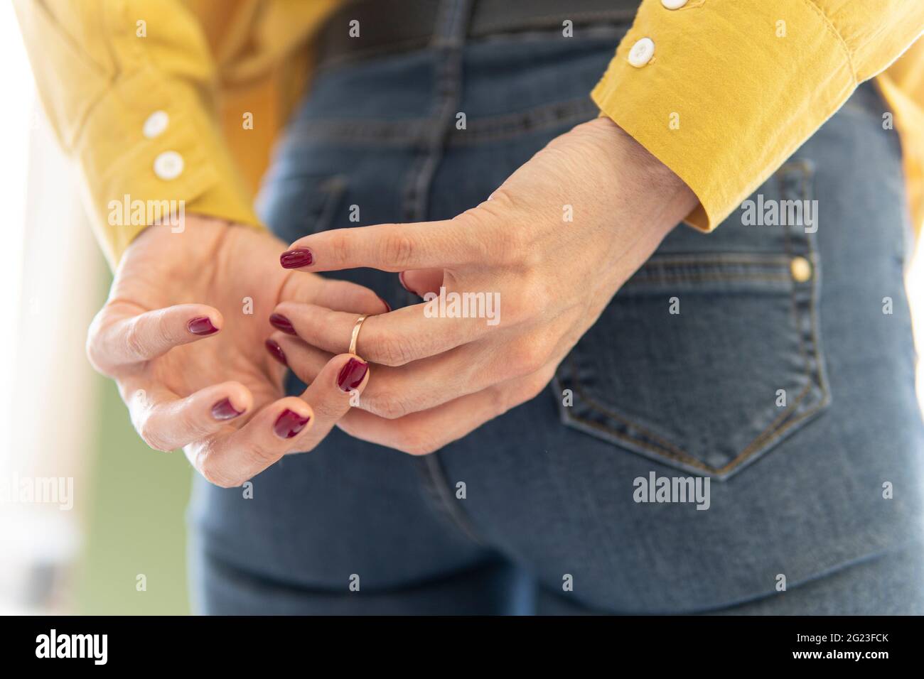 une femme qui lutte pour enlever l'anneau de mariage de son doigt tenant les mains derrière son dos. retirez l'anneau de votre doigt. Le concept de trahison a Banque D'Images