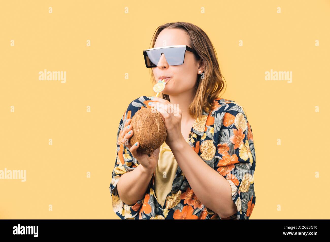 jeune femme dans une chemise fleurie et de grandes lunettes de soleil  buvant un cocktail de noix de coco avec une paille sur fond jaune Photo  Stock - Alamy