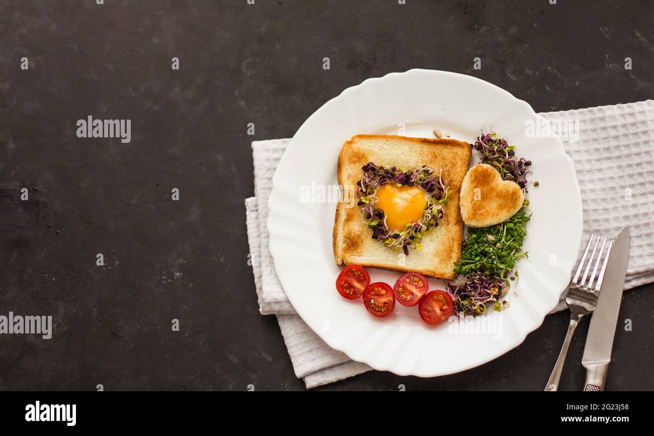 Oeuf dans un trou de pain en forme de coeur, microverts, nourriture saine petit déjeuner, thé, fond noir Banque D'Images