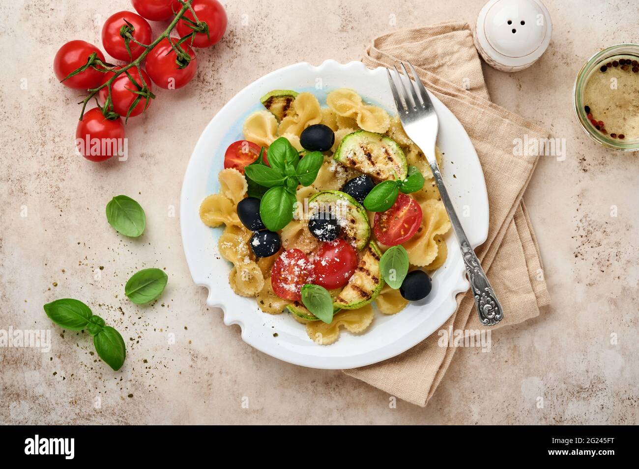 Pâtes salade fiocchi aux légumes courgettes grillées, tomates cerises, olives, basilic et parmesan dans une assiette blanche sur ardoise légère, pierre ou bétons Banque D'Images