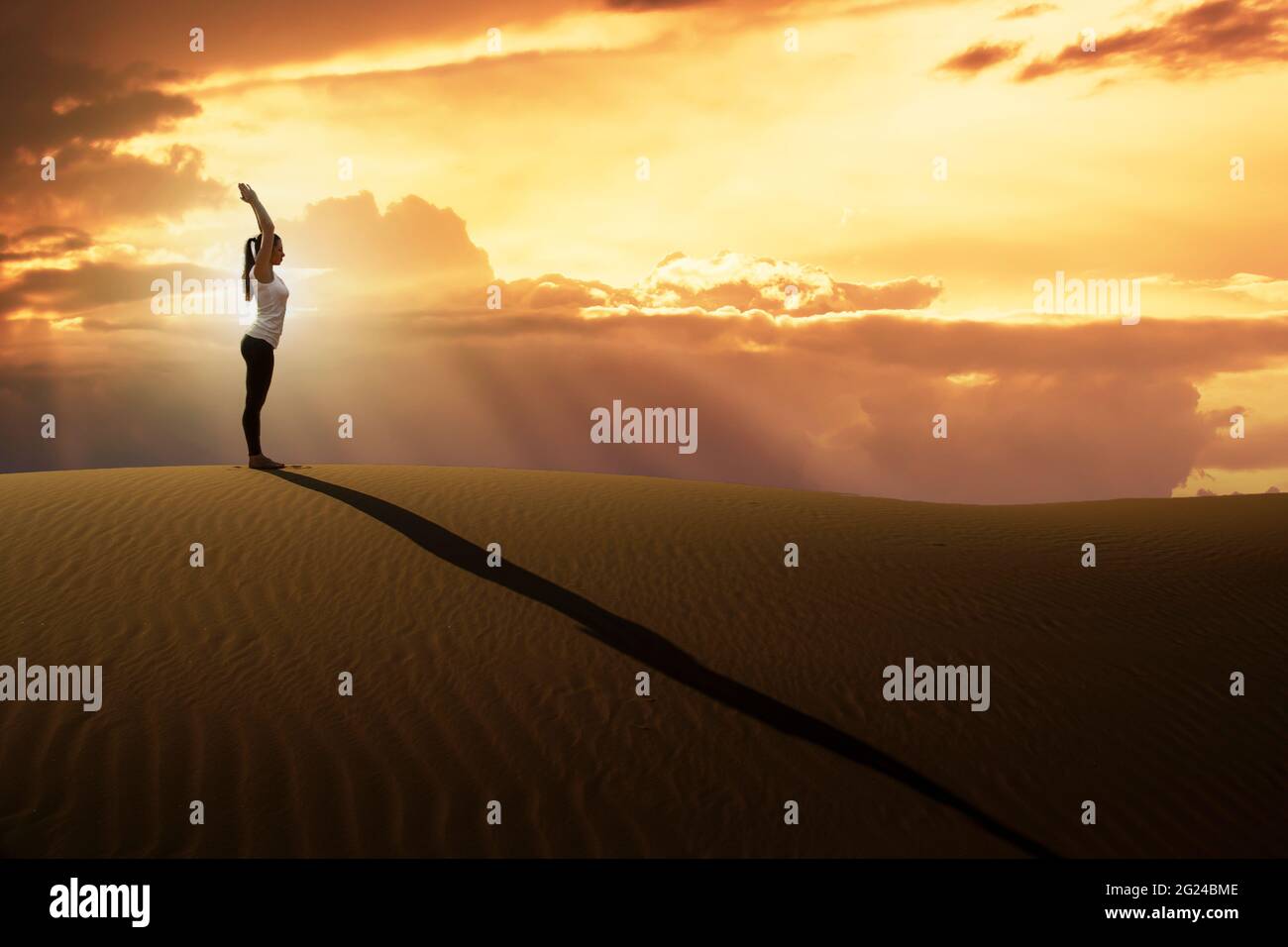 Dubaï, Émirats arabes Unis, femme pratiquant le yoga sur une dune de sable dans le désert au coucher du soleil Banque D'Images