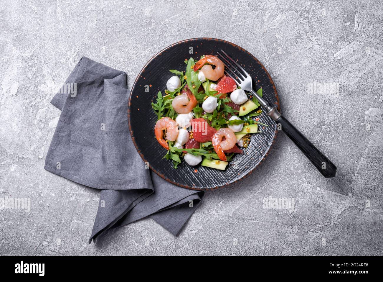 Vue de dessus de la nourriture saine et savoureuse. Salade de feuilles d'arugula fraîches, fromage mozzarella, crevettes, pamplemousse, avocat et sauce moutarde sur bétons gris Banque D'Images