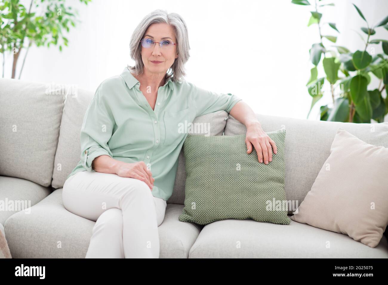 Photo de charmante sérieuse calme vieille femme s'asseoir canapé week-end porte des lunettes à l'intérieur de la maison appartement Banque D'Images