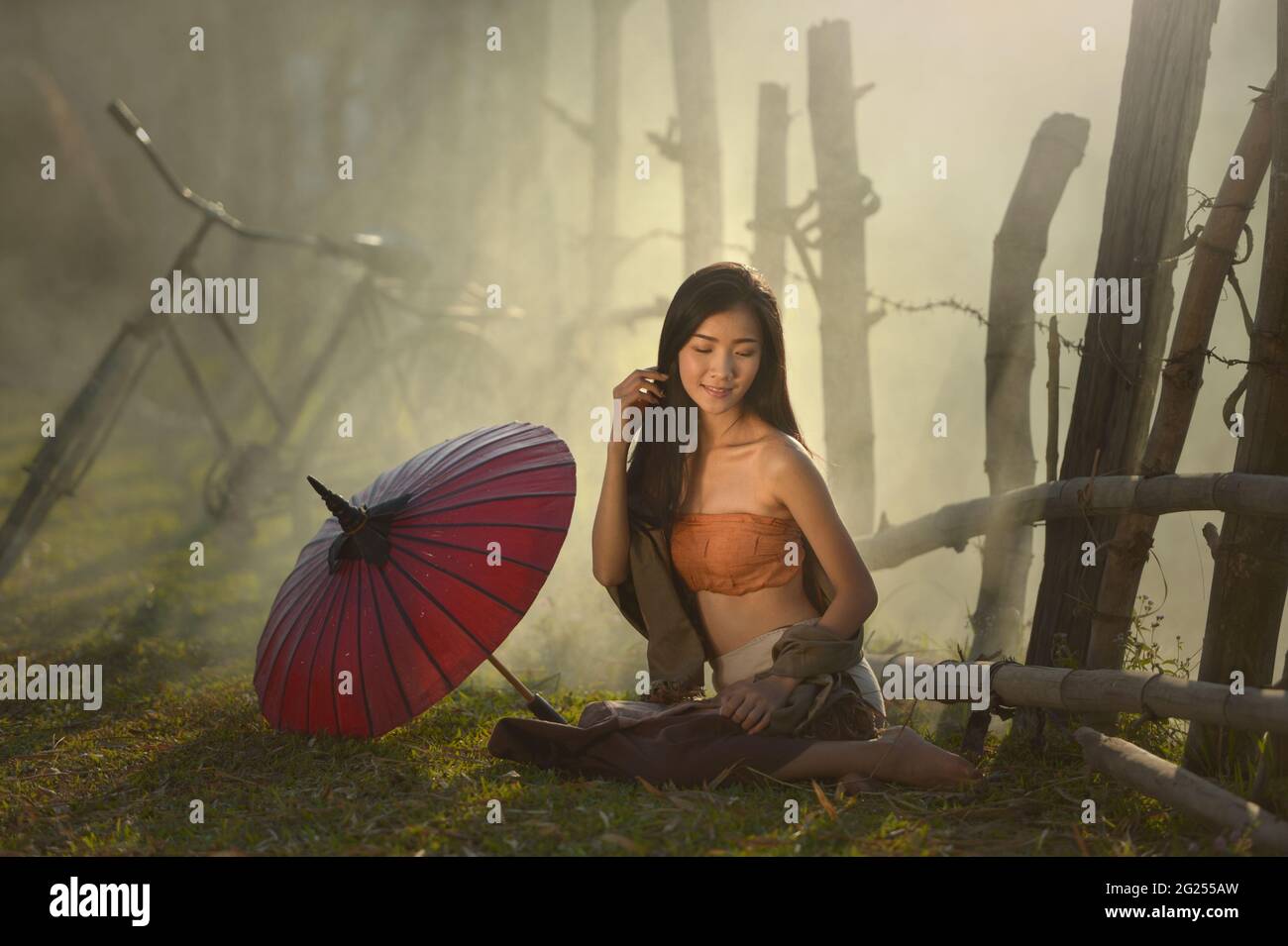 Femme assise sur l'herbe à côté de son parasol, Thaïlande Banque D'Images