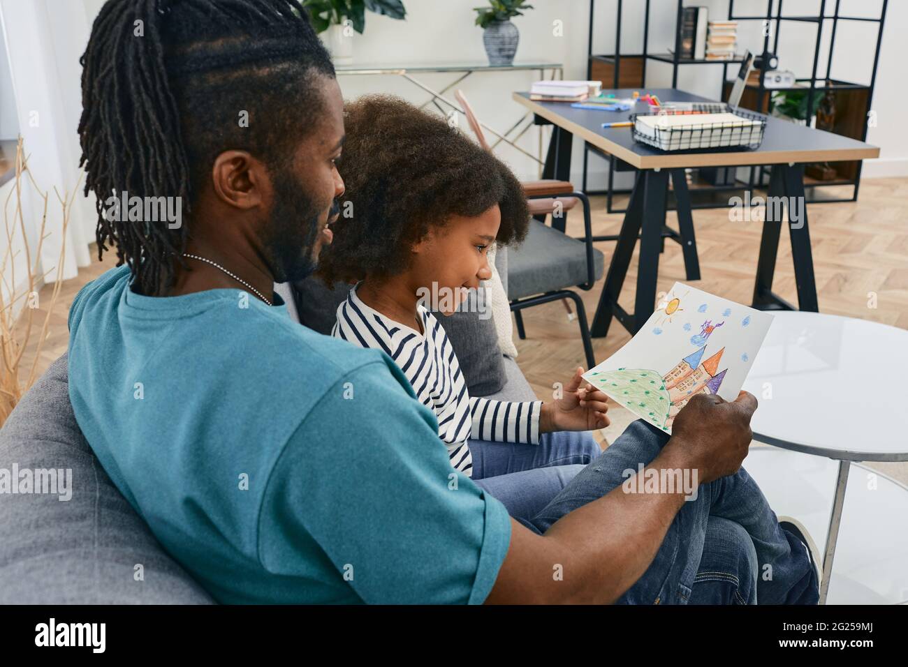 Papa et sa fille passent du temps ensemble le jour du Père. Famille afro-américaine assise sur un canapé et regardant le dessin de l'enfant, la convivialité Banque D'Images