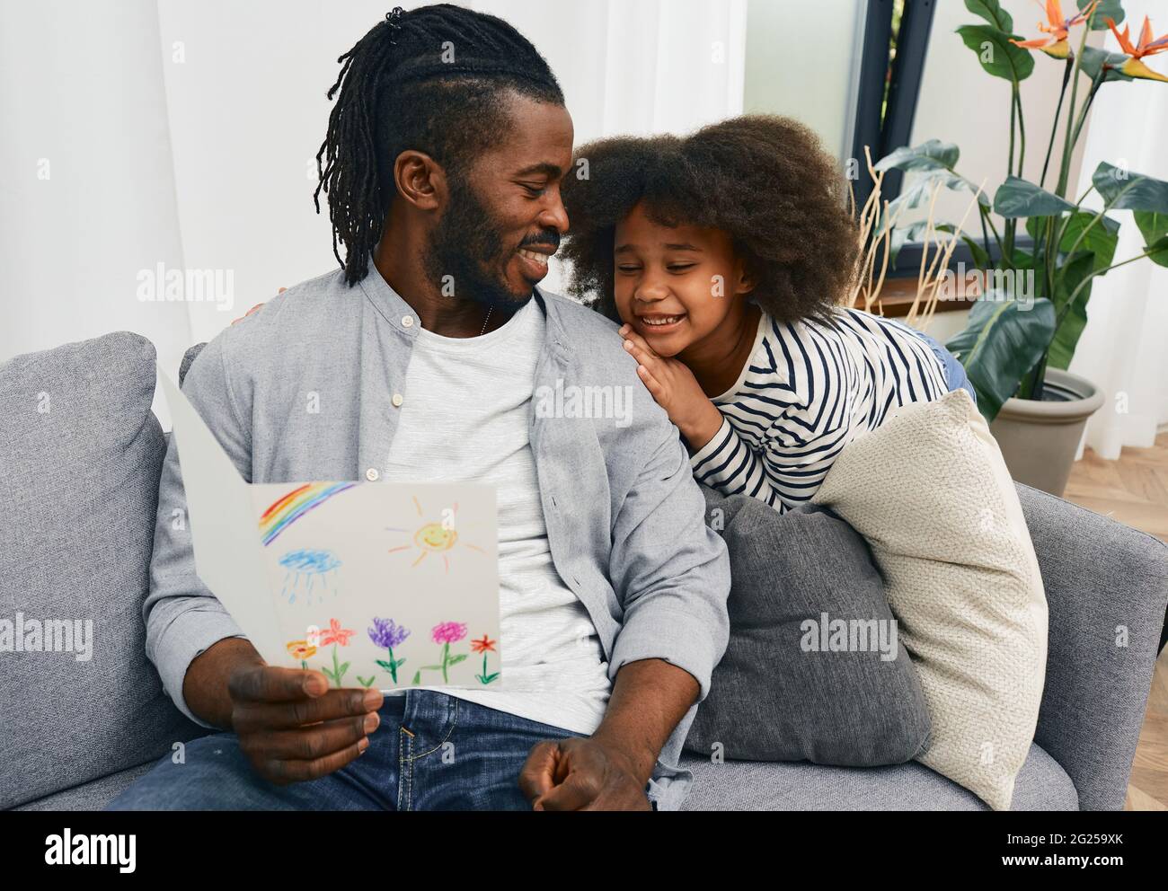 Relation père-fille. Papa est heureux de recevoir une carte de voeux avec un dessin d'enfant de sa fille à la fête du père, assis sur un canapé à h Banque D'Images