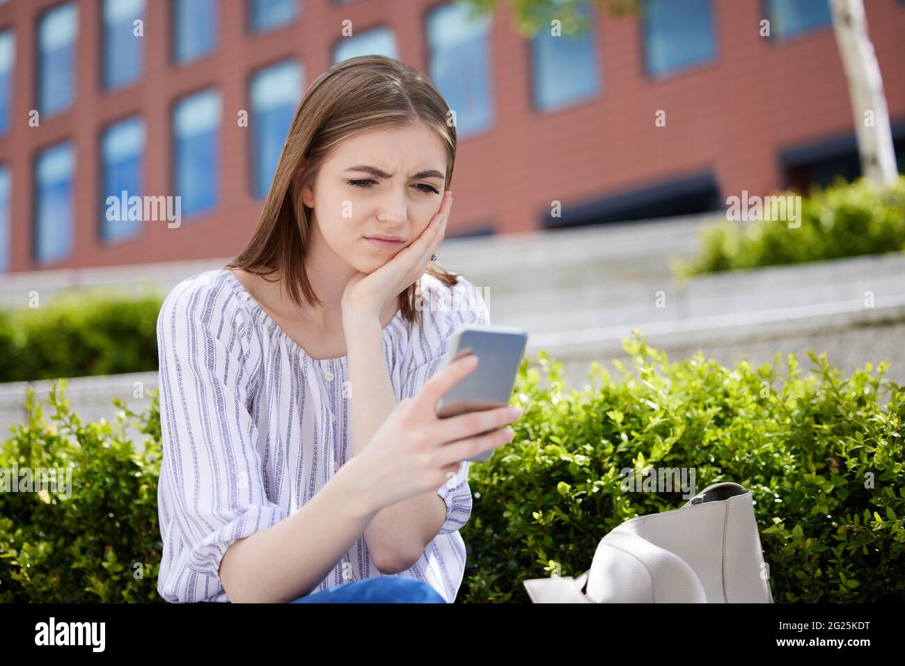 Une jeune femme malheureuse avec le téléphone mobile victime d'intimidation en ligne sur le campus d'Universtiy Banque D'Images