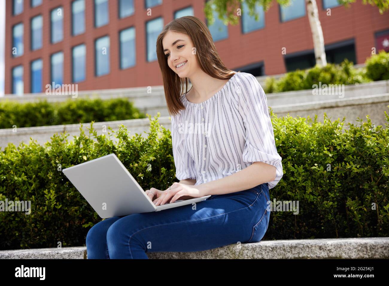 Jeune étudiante au collège avec ordinateur portable travaillant à l'extérieur sur le campus du collège Banque D'Images
