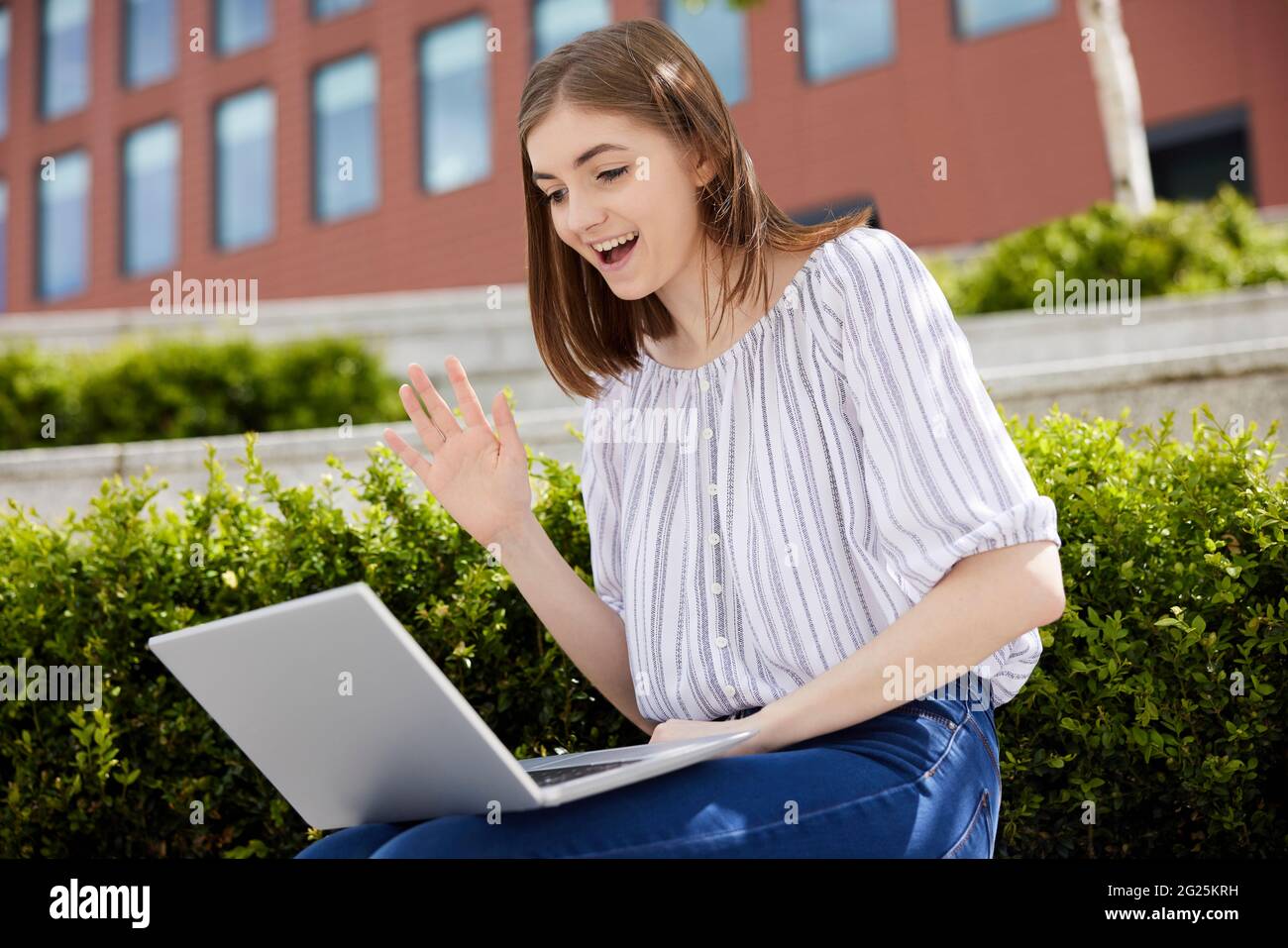 Jeune femme étudiant ou employé de bureau avec ordinateur portable ayant le chat vidéo à l'extérieur sur le campus de l'université Banque D'Images
