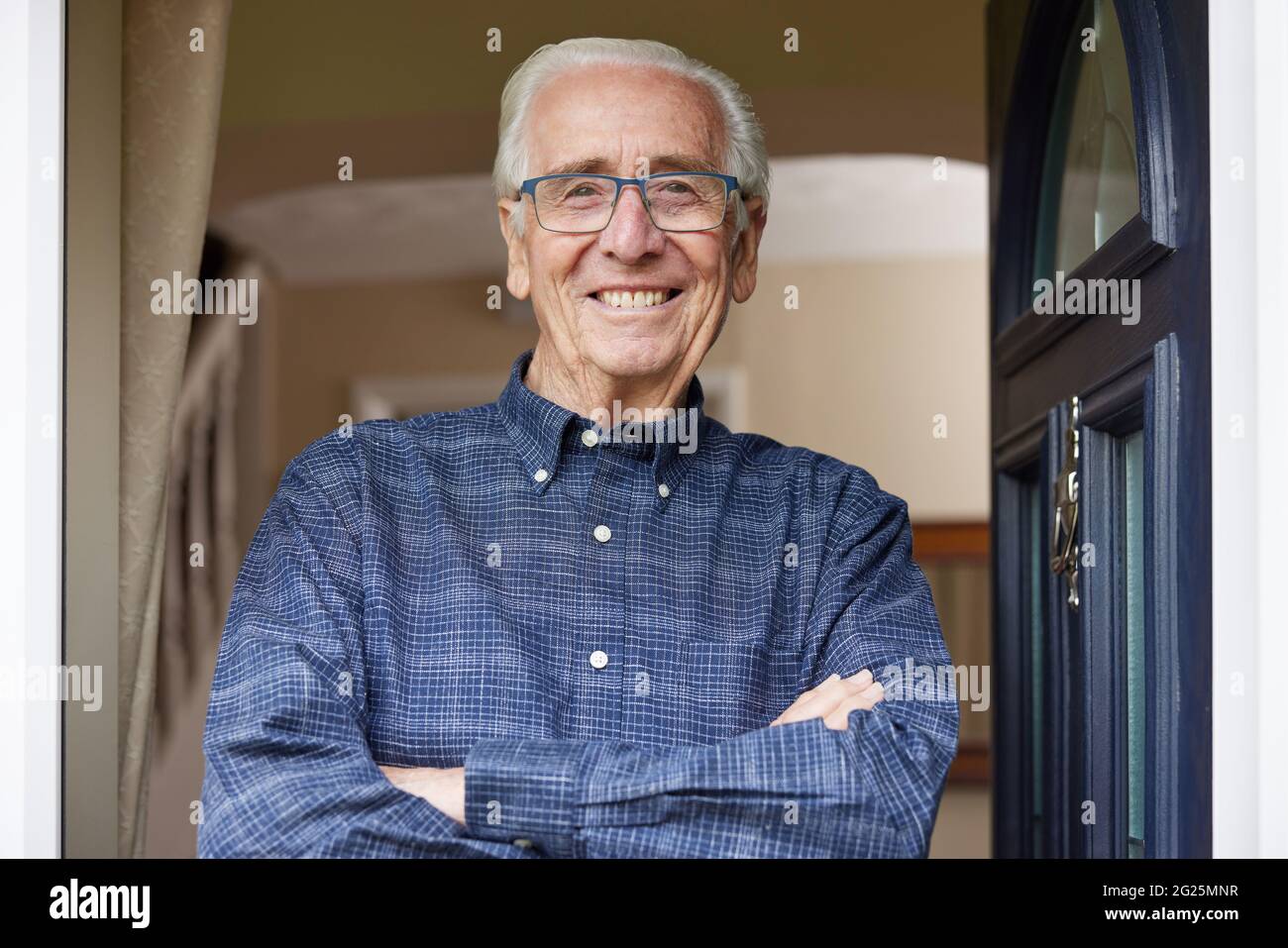 Portrait de l'homme senior souriant debout à la porte ouverte de la maison Banque D'Images