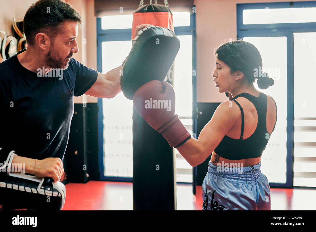 Une jeune femme s'entraîne avec son entraîneur Muay Thai dans une salle de sport Banque D'Images