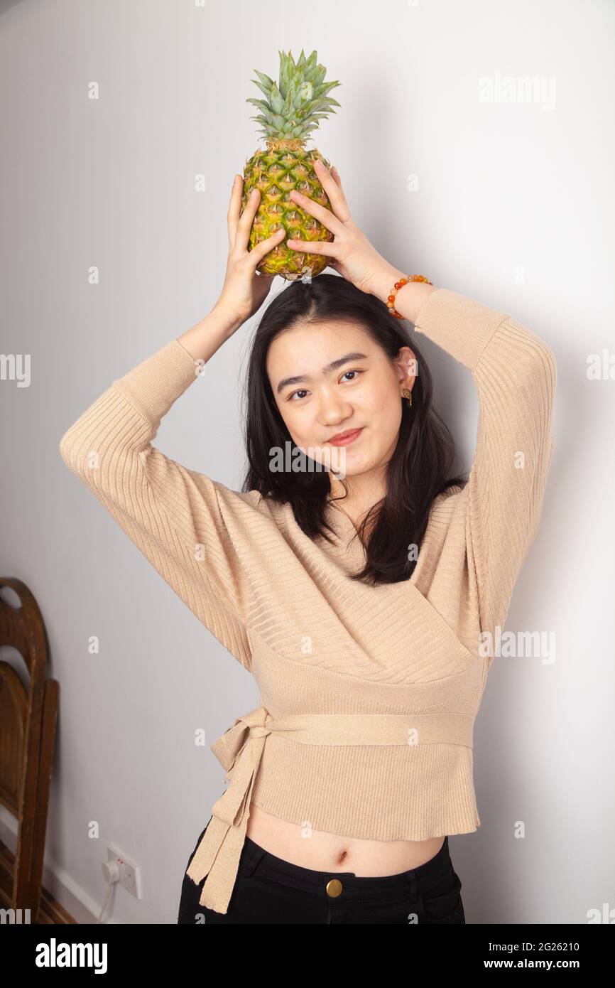 Jeune femme asiatique tenant un ananas sur sa tête Banque D'Images