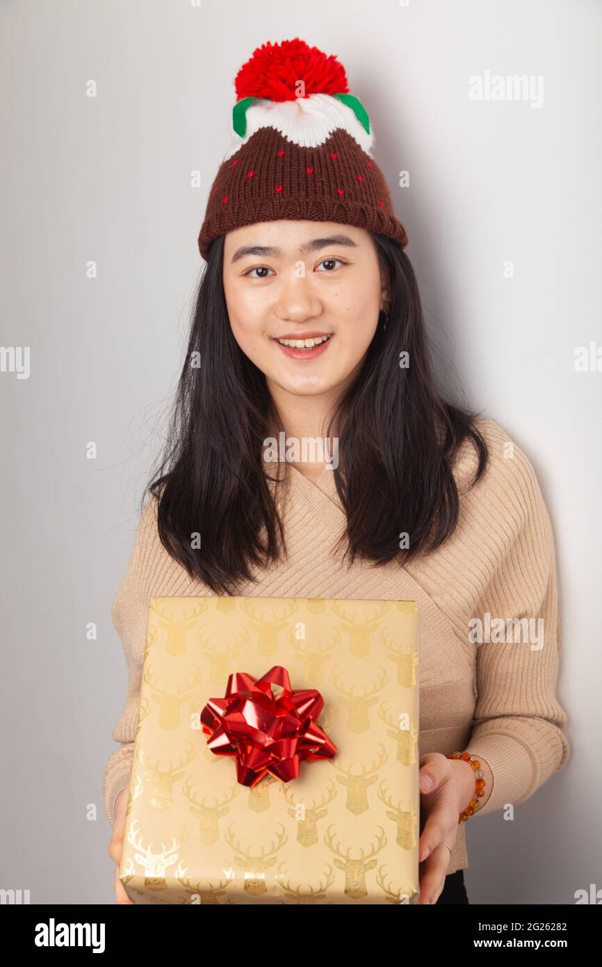 Une femme asiatique portant un chapeau de pudding de Noël et tenant un cadeau de noël. Banque D'Images