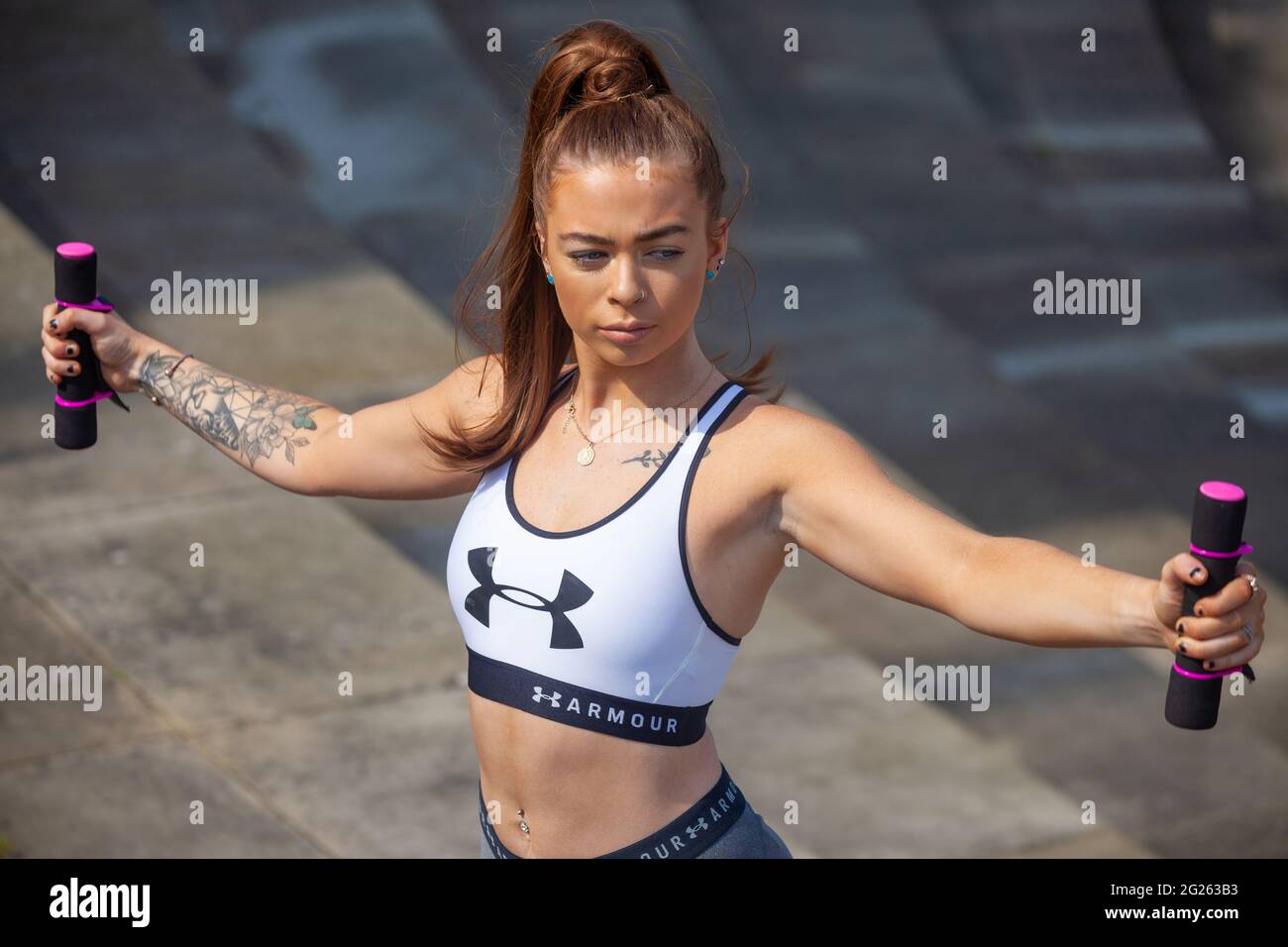 Jeune femme portant des vêtements de sport avec ses bras tendus tenant des poids Banque D'Images