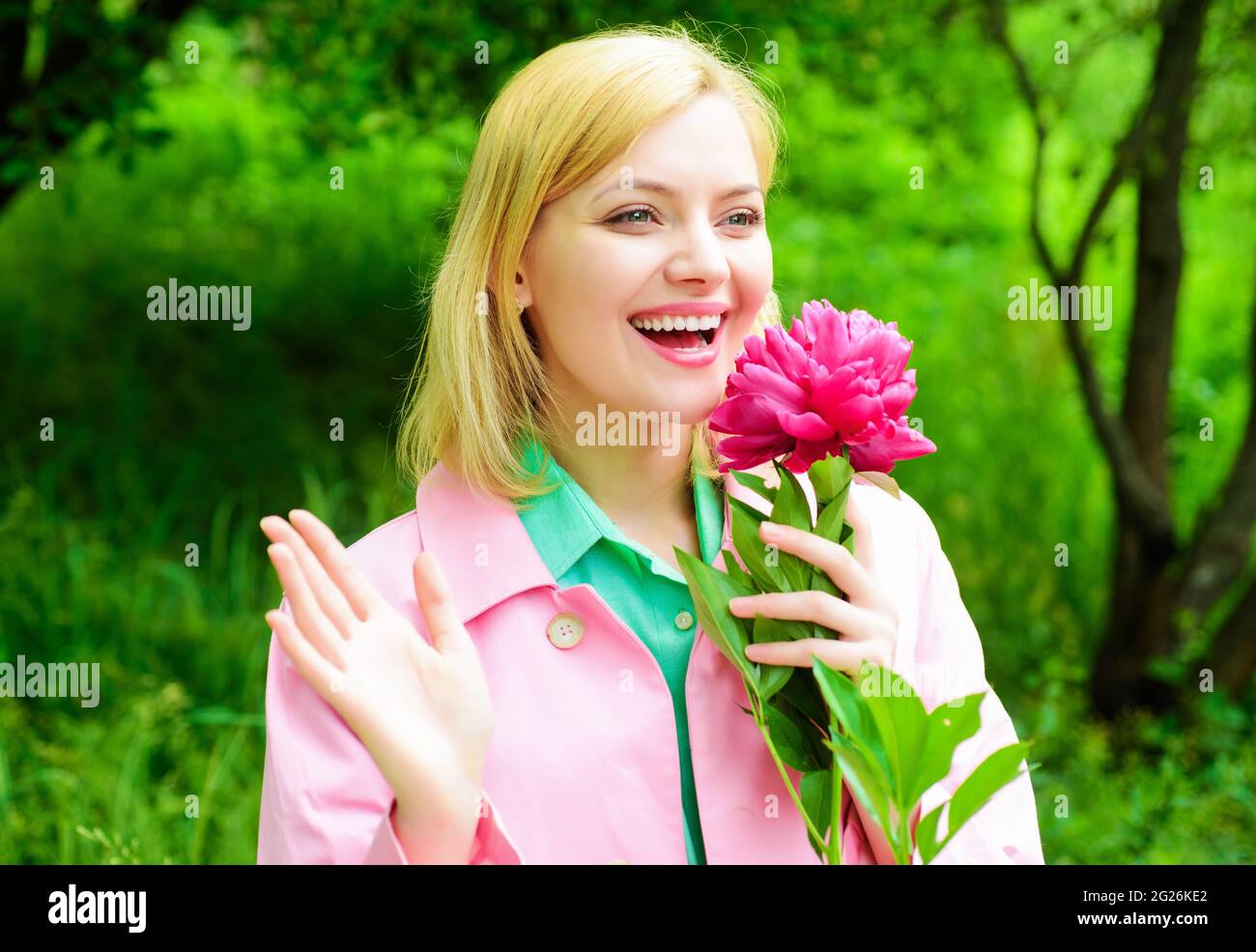 Femme blonde souriante avec fleur de pivoine à l'extérieur. Belle fille dans le jardin. Banque D'Images