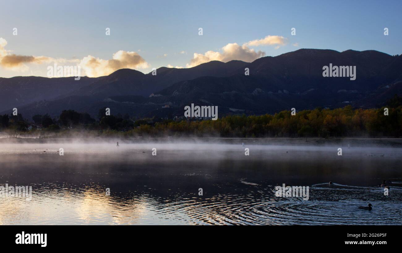 La brume plane sur la surface du lac avec des montagnes en arrière-plan. Banque D'Images