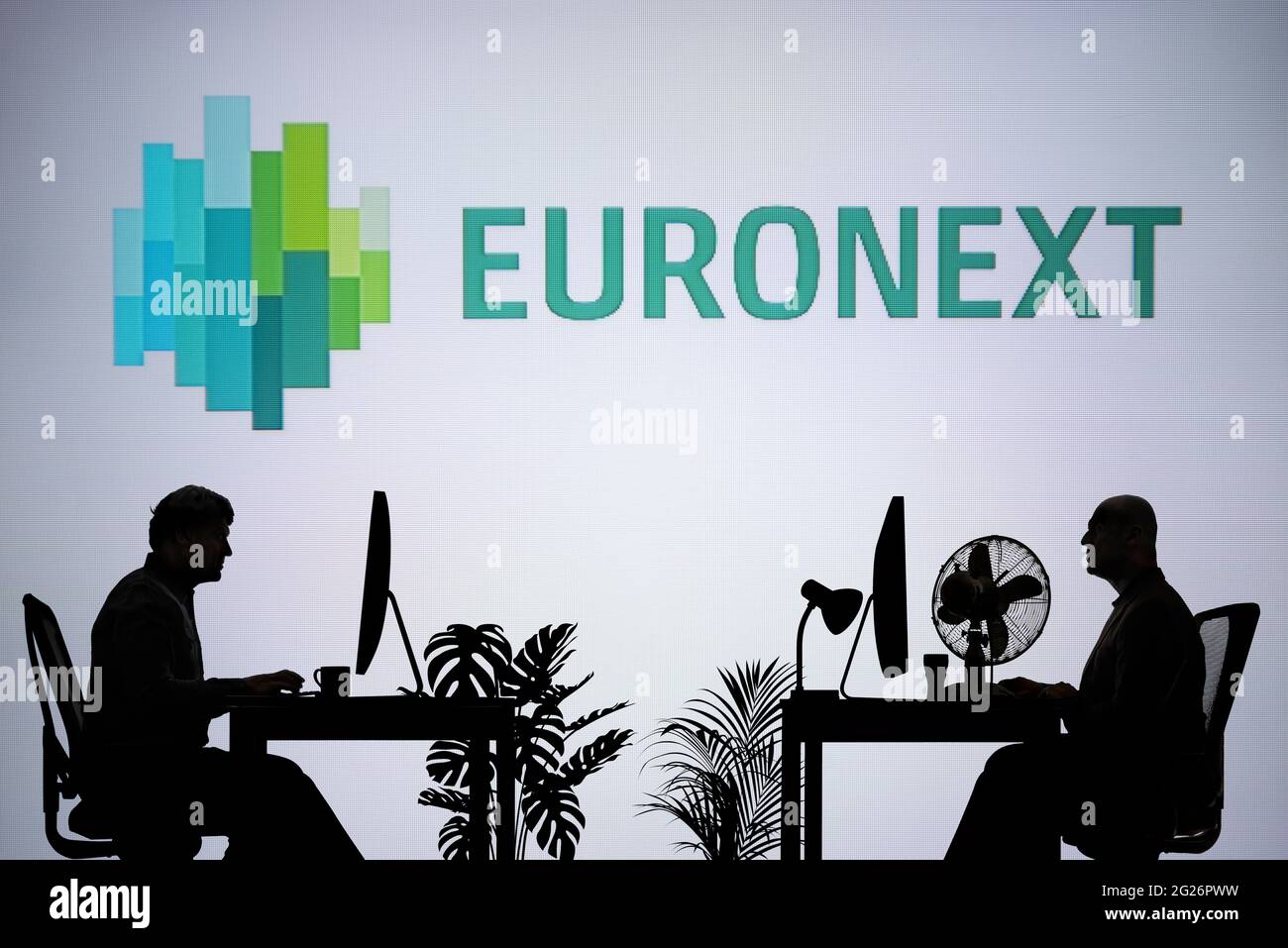 Le logo Euronext est visible sur un écran LED en arrière-plan tandis que deux personnes silhouetées travaillent dans un environnement de bureau (usage éditorial uniquement) Banque D'Images