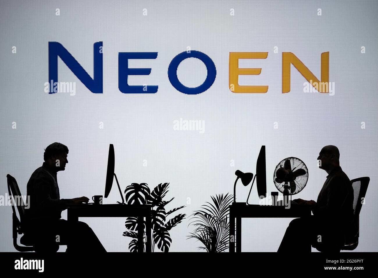 Le logo Neoen est visible sur un écran LED en arrière-plan tandis que deux personnes silhouetées travaillent dans un environnement de bureau (usage éditorial uniquement) Banque D'Images