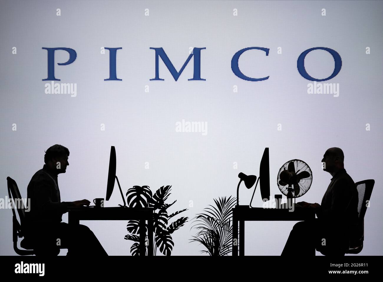 Le logo PIMCO est visible sur un écran LED en arrière-plan tandis que deux personnes silhouetées travaillent dans un environnement de bureau (usage éditorial uniquement) Banque D'Images