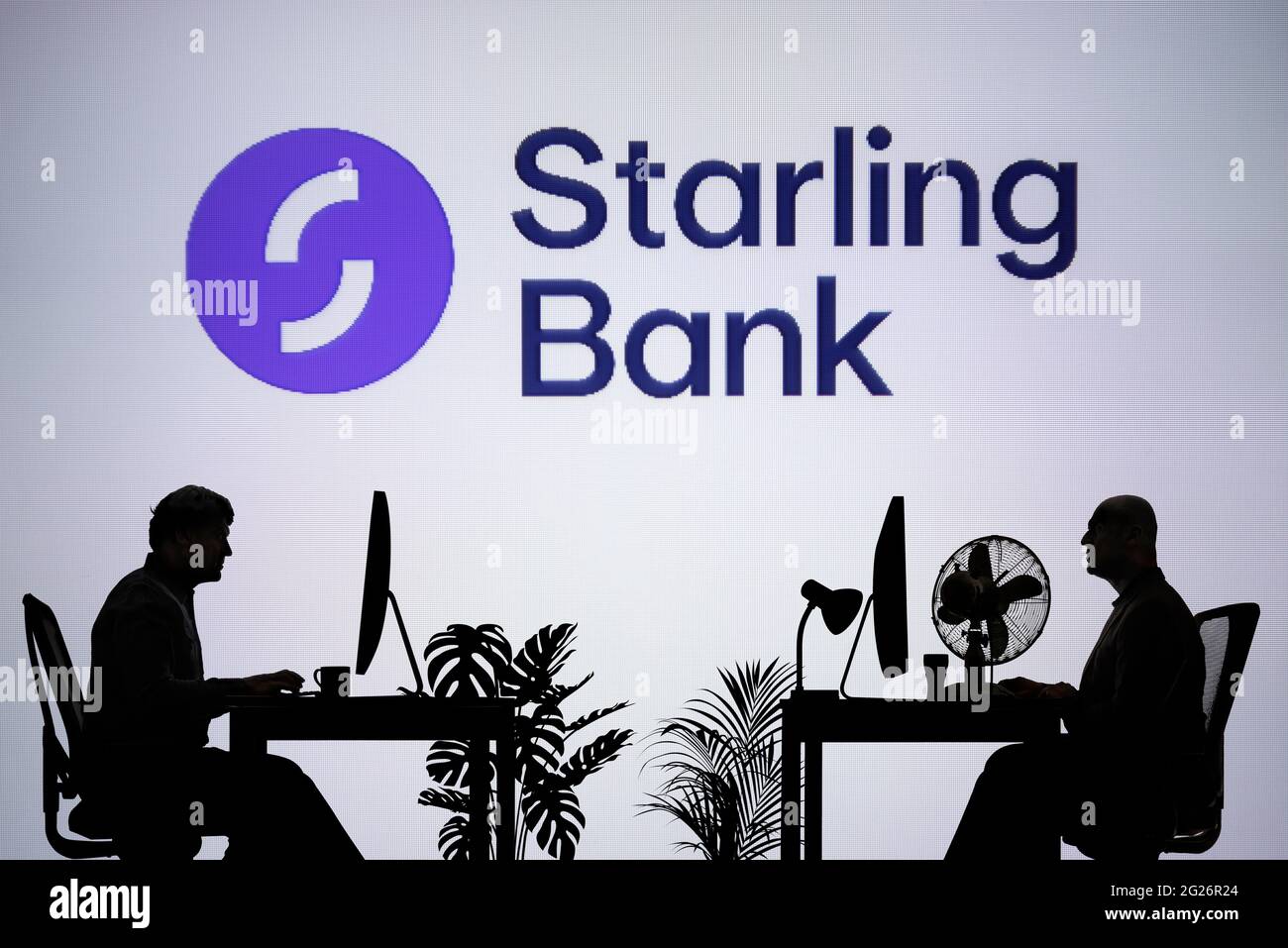 Le logo Starling Bank est visible sur un écran LED en arrière-plan tandis que deux personnes silhouetées travaillent dans un environnement de bureau (usage éditorial uniquement) Banque D'Images