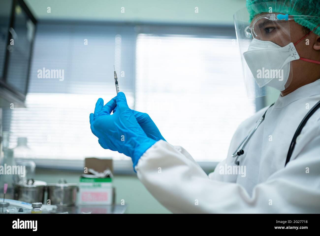 Le jeune médecin, vêtu d'un uniforme blanc et portant un masque facial, prépare une seringue pour vacciner les personnes du centre médical. Banque D'Images
