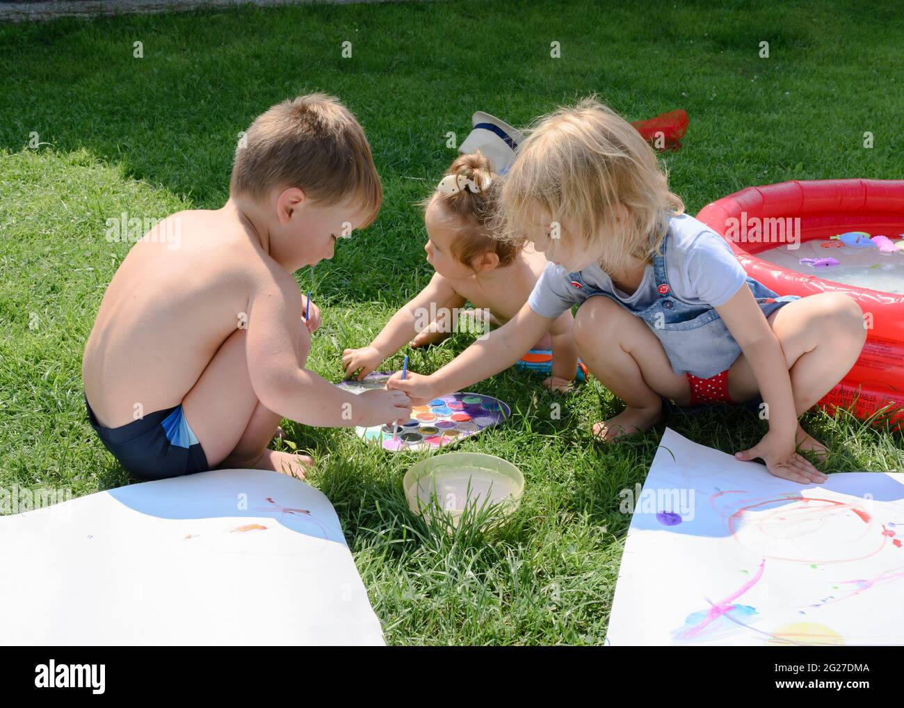 Les enfants sur la pelouse ensoleillée devant la maison peignent avec des peintures Banque D'Images