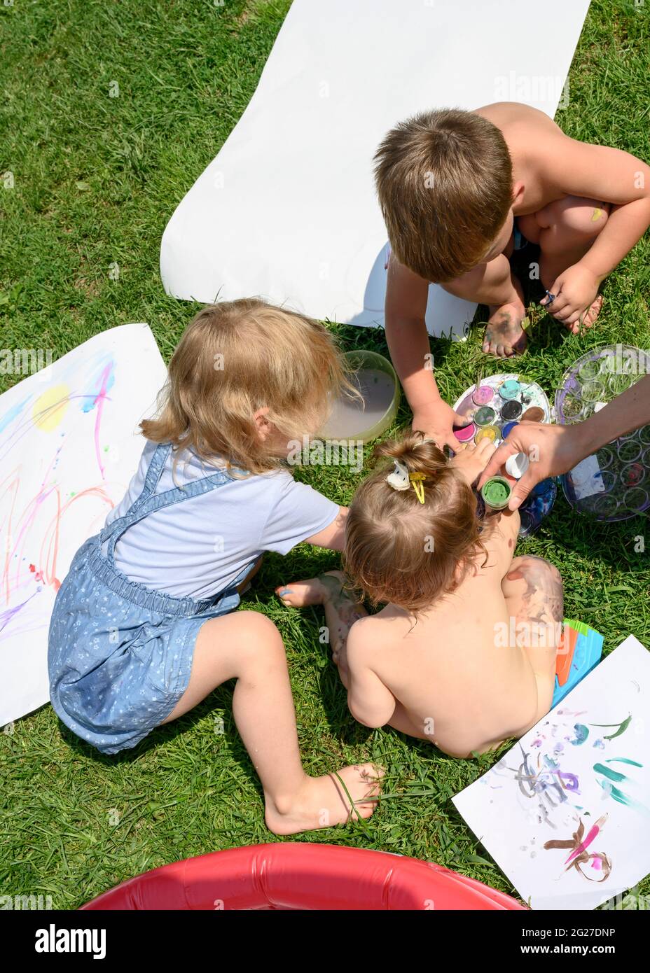 Les enfants sur la pelouse ensoleillée devant la maison peignent avec des peintures Banque D'Images