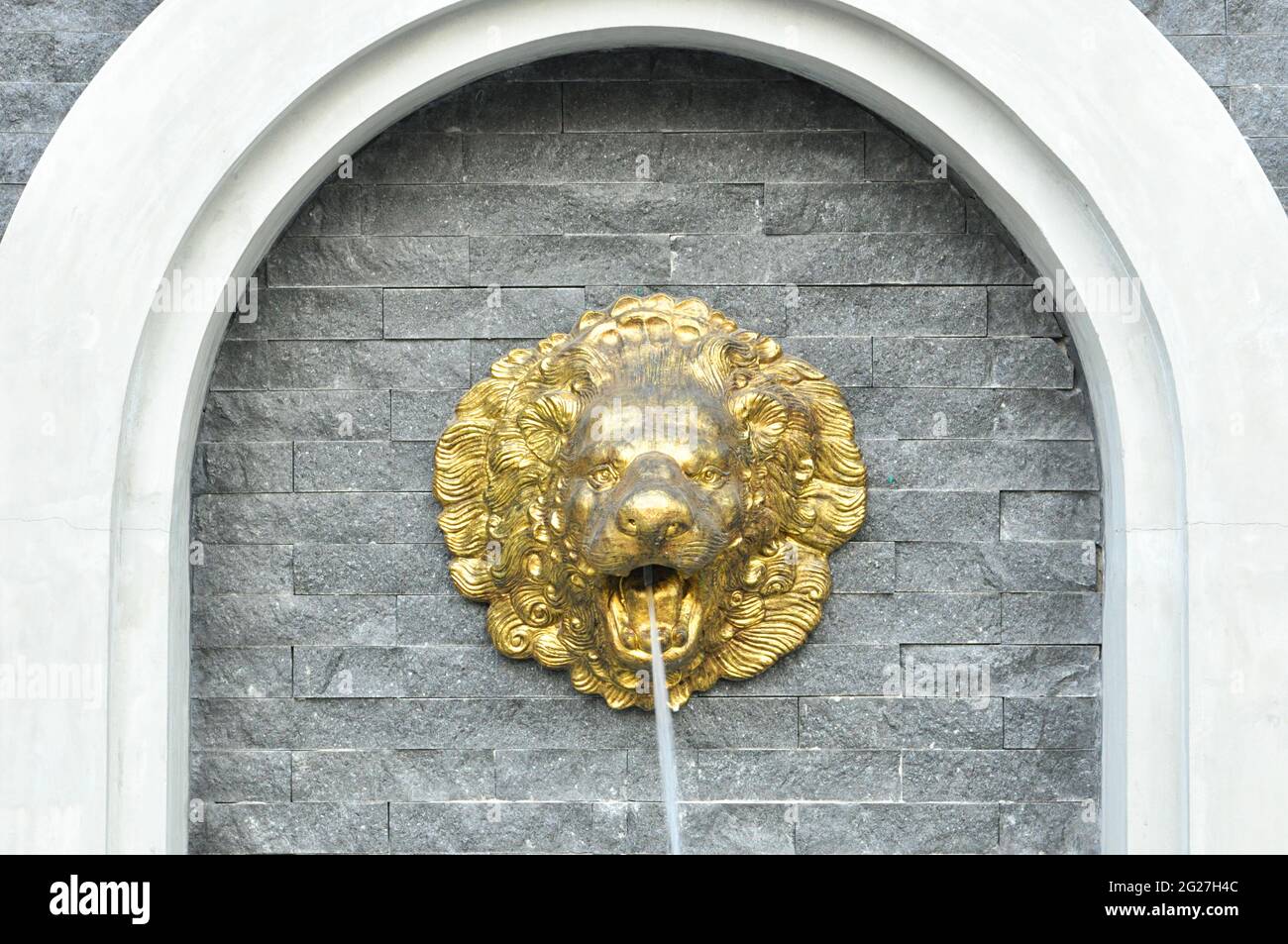 Sculpture à tête de lion dorée sur un mur en pierre qui jaillissent de l'eau Banque D'Images