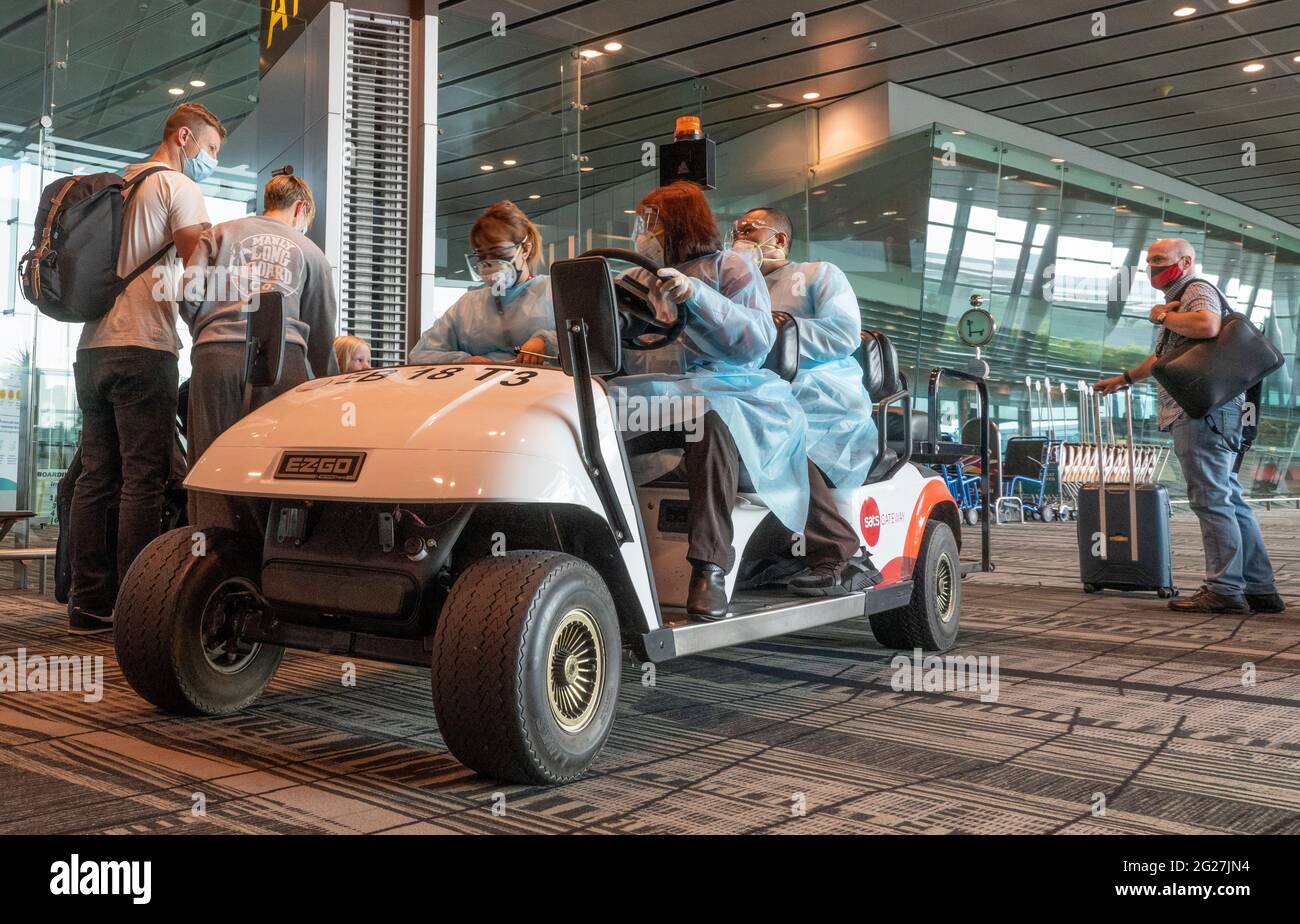 Singapour, 8 juin 2021 - les passagers se préparent à embarquer pour un vol à destination de Londres à l'aéroport Changi de Singapour, tandis que le personnel de l'aéroport chargé de l'équipement de protection individuelle transporte un passager âgé dans une voiturette de golf. Tous les travailleurs de l'aéroport portent des blouses, des masques et des lunettes de protection dans les terminaux d'arrivée et de départ. Avant la pandémie de Covd-19, en 2019, l'aéroport de Changi était le septième aéroport le plus occupé par le trafic international de passagers dans le monde et le troisième en Asie. Crédit : Rob Taggart/Alay Live News Banque D'Images