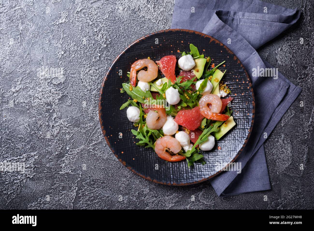 Vue de dessus de la nourriture saine et savoureuse. Salade de feuilles d'arugula fraîches, fromage mozzarella, crevettes, pamplemousse, avocat et sauce moutarde sur bétons gris Banque D'Images