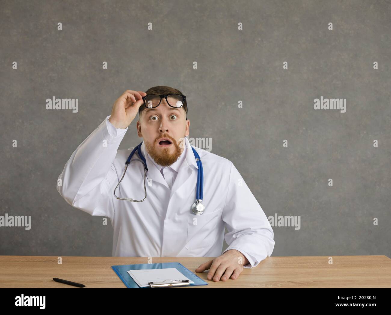 Un médecin choqué, un professionnel de la santé, prend des lunettes, s'assoit au bureau et regarde la caméra Banque D'Images