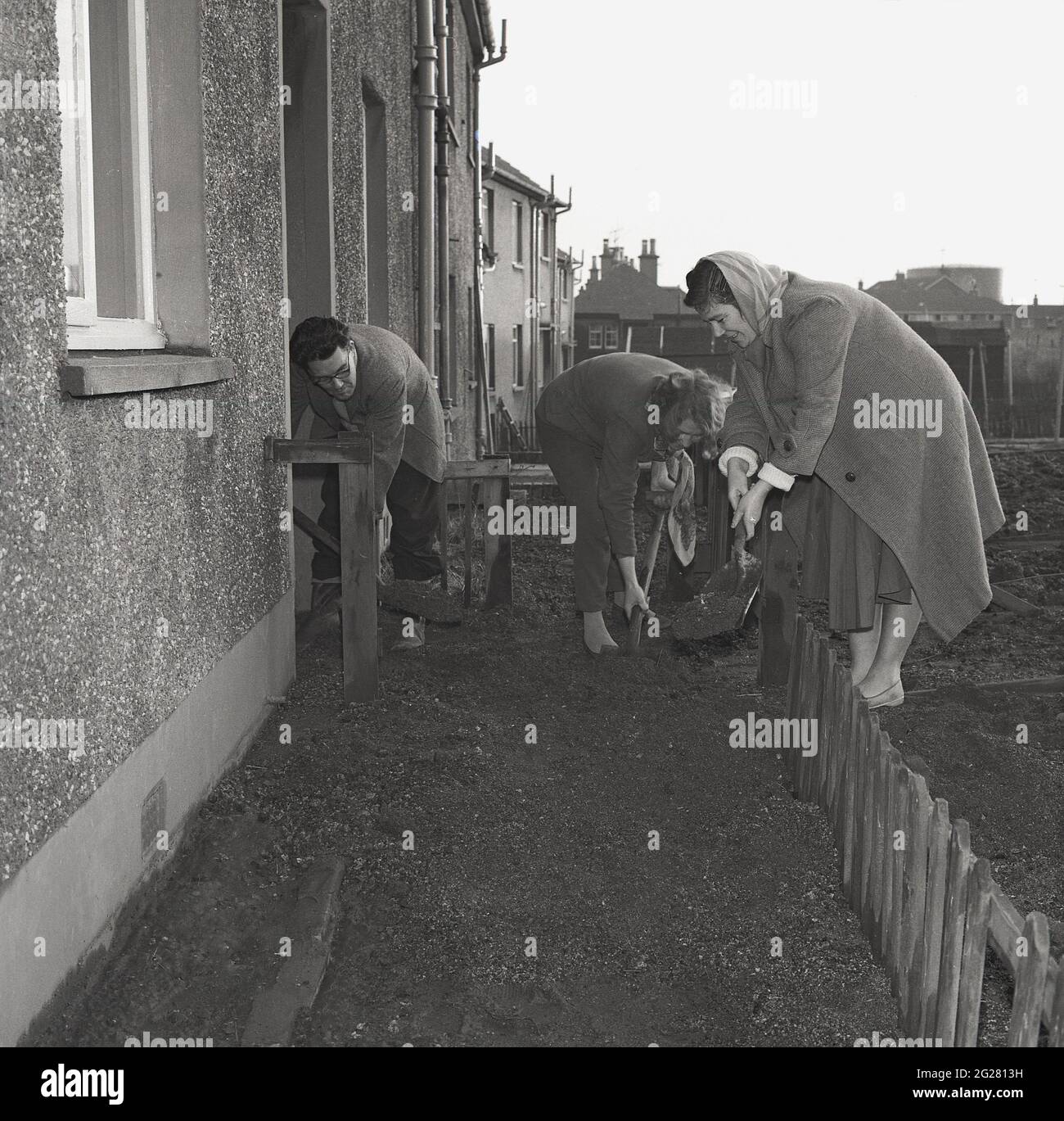 Années 1960, historique, à l'extérieur d'une maison mitoyenne, un homme et deux femmes avec des bêches qui se délaient pour construire un chemin, posant des sols pour les fondations des dalles de pavage, Kelty, Fife, Écosse, Royaume-Uni. Un village minier de charbon sur la frontière de Fife et de Perthshire, à cette époque, les villageois ont dû faire face à un avenir économique incertain, comme les mines de charbon, Qui employait autrefois la majorité des travailleurs locaux à partir de 1873 depuis la fermeture de la première mine profonde, la mine Lindsey. Banque D'Images