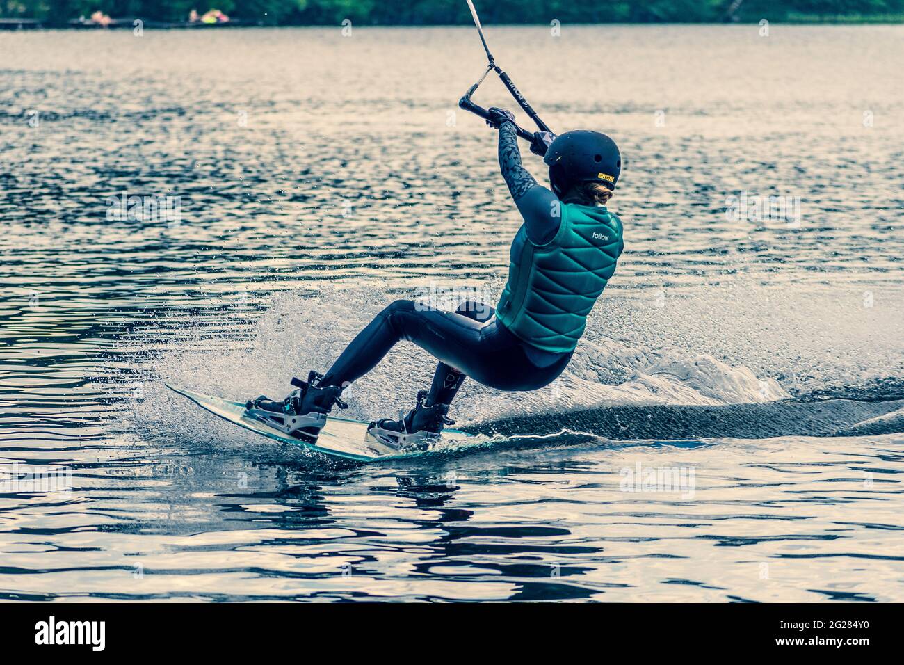 Une fille avec un casque et un gilet de sauvetage fait un wakeboard sur le  lac avec forêt en arrière-plan, wakeboard, sports nautiques en été Photo  Stock - Alamy