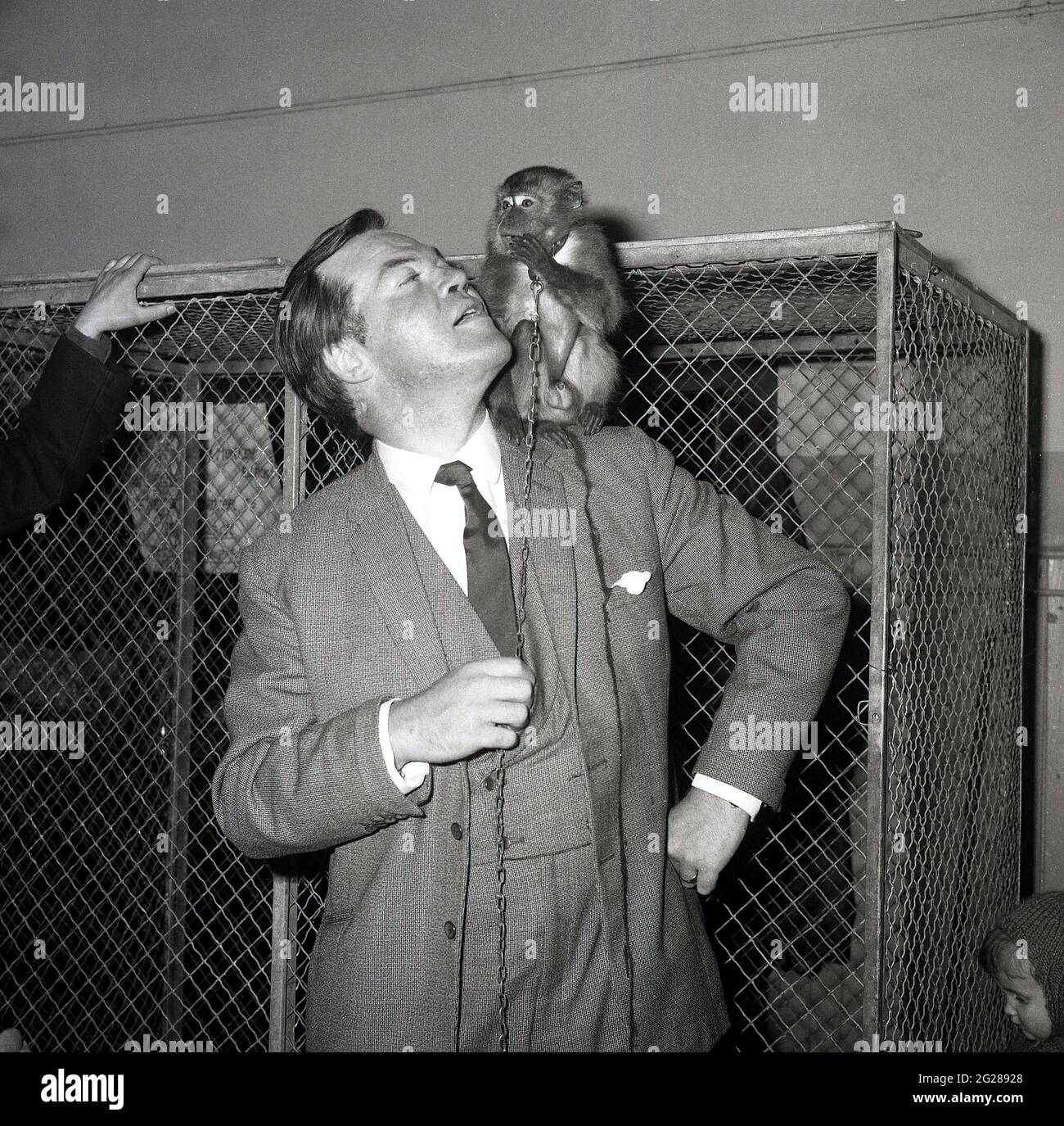 Années 1960, historique, devant une cage métallique, homme bien habillé dans un costume à carreaux de trois pièces avec un petit singe sur son épaule, Écosse, Royaume-Uni. Bill Tennent était une personnalité de premier plan dans les premières années de la télévision écossaise. Il était toujours prêt à tourner la main vers tout, y compris la religion, l'éducation et les documentaires. Plusieurs salons de discussion ont été construits autour de lui, y compris le Bill Tennent Show et Time Out avec Tennent. Banque D'Images