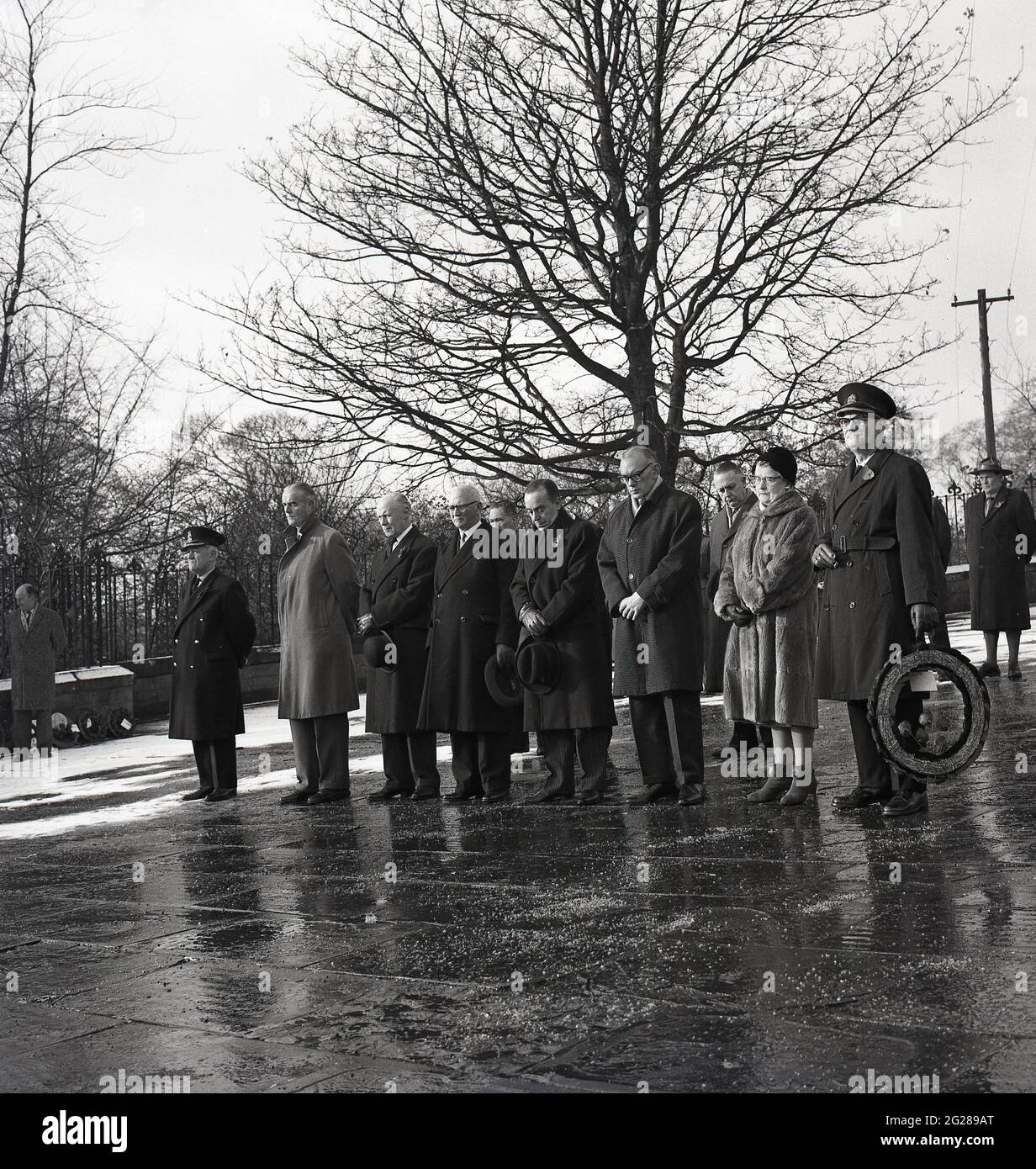 Années 1960, historique, jour de souvenir, debout à l'extérieur lors d'un hiver froid, un petit groupe d'hommes et une femme se sont inclinés la tête en l'honneur de ceux qui ont combattu et sont morts dans les deux guerres mondiales, Kelty, Fife, Écosse, Royaume-Uni. Banque D'Images