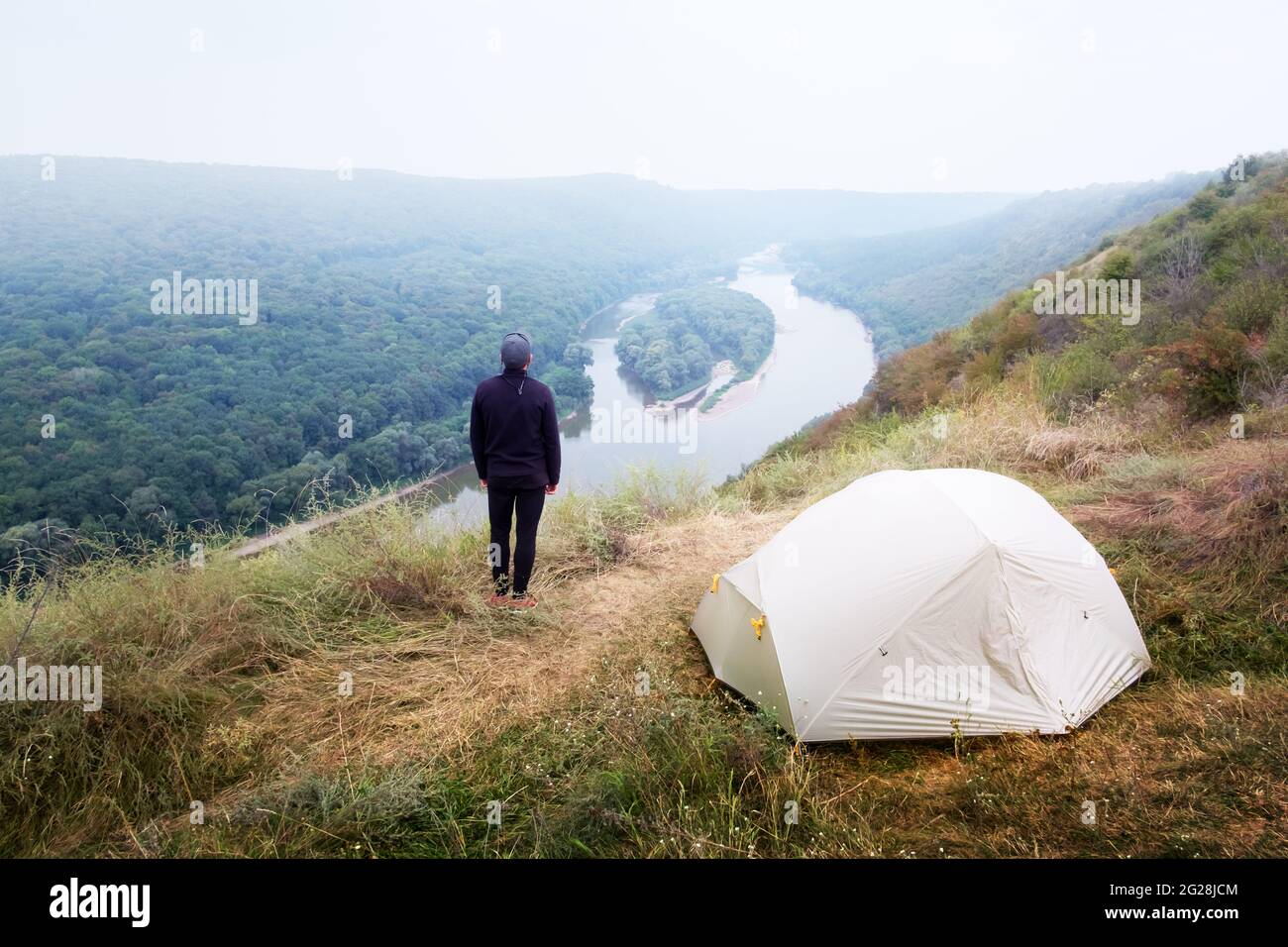 Un touriste se tient près d'une tente au sommet d'une montagne au-dessus du majestueux fleuve Dniester en Ukraine. Photographie de paysage Banque D'Images