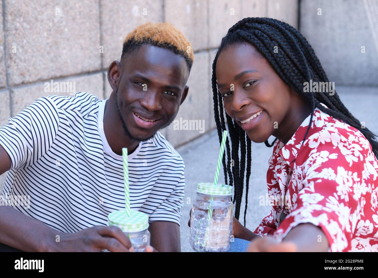 Jeune couple heureux noir prenant un selfie, buvant des rafraîchissements et assis sur les escaliers. Concept de vie urbaine. Banque D'Images