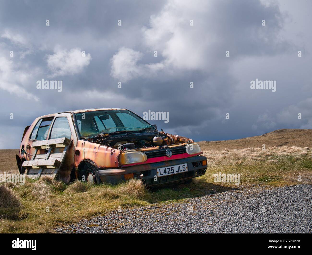Un golf abandonné, blanc, 1993 VW maintenant coloré avec de la rouille se décompose dans un cadre rural. Pris par une journée ensoleillée avec des nuages de pluie qui s'amassent. Banque D'Images