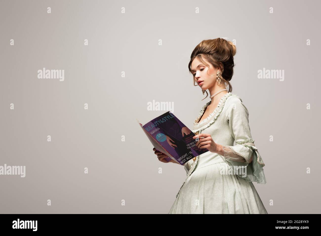 charmante femme en robe vintage lisant magazine moderne isolé sur gris Banque D'Images