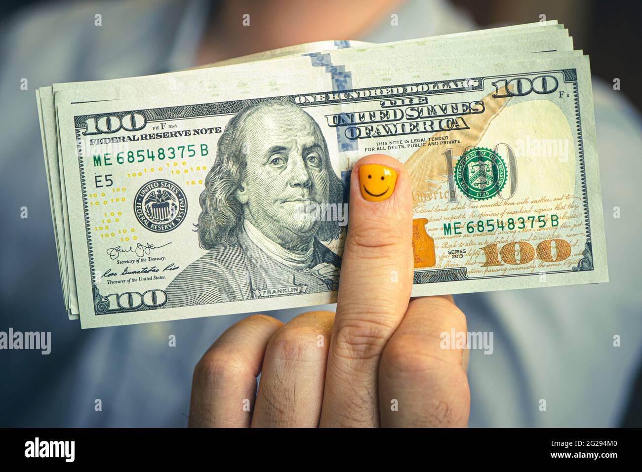Joyeux jeune homme avec des dollars. L'homme d'affaires tient l'argent dans sa main. Un drôle de visage smiley est dessiné sur l'ongle jaune. Le concept de revenu élevé Banque D'Images