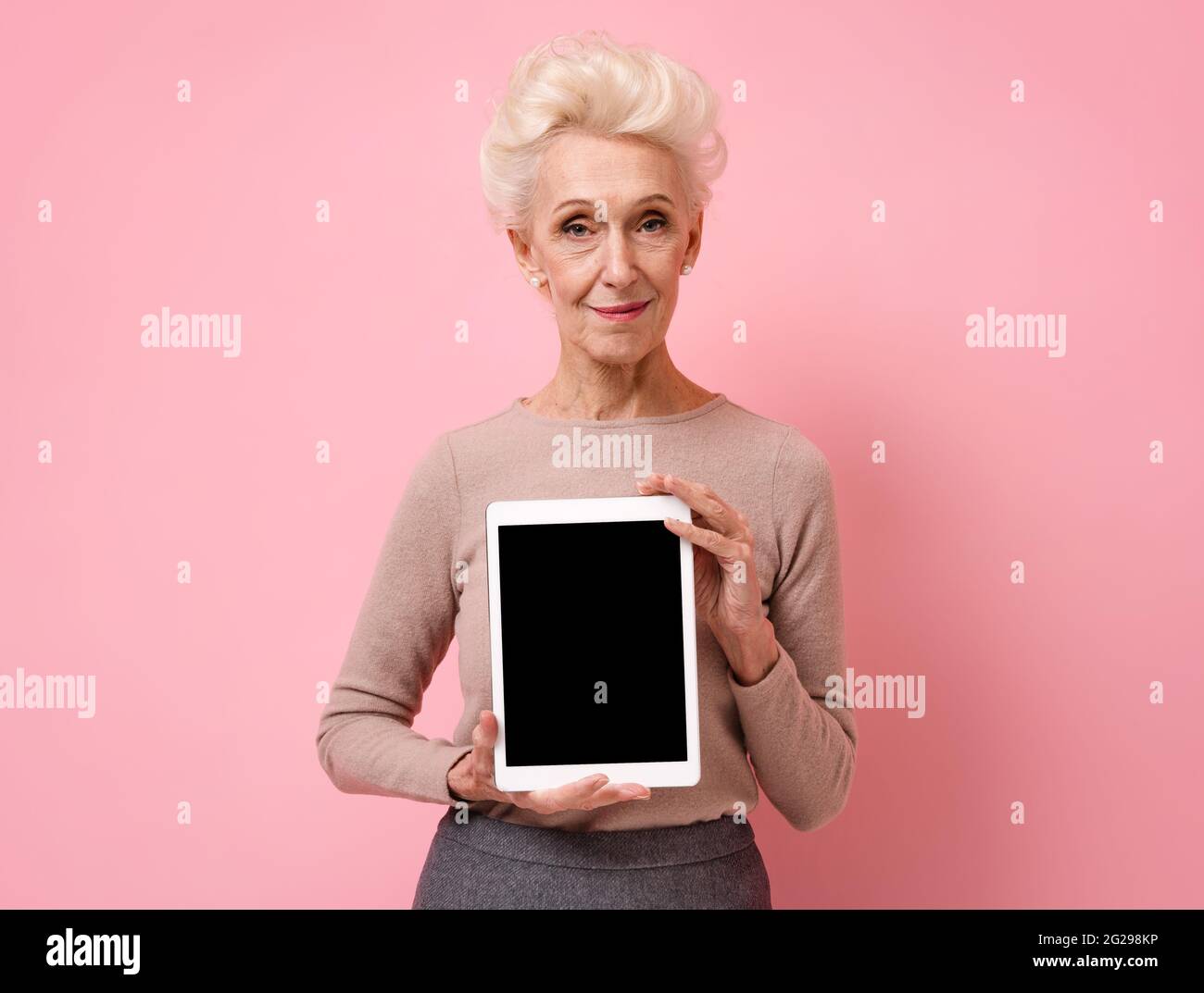 Femme souriante tenant une tablette numérique avec un écran vierge. Photo d'une femme âgée sur fond rose. Banque D'Images