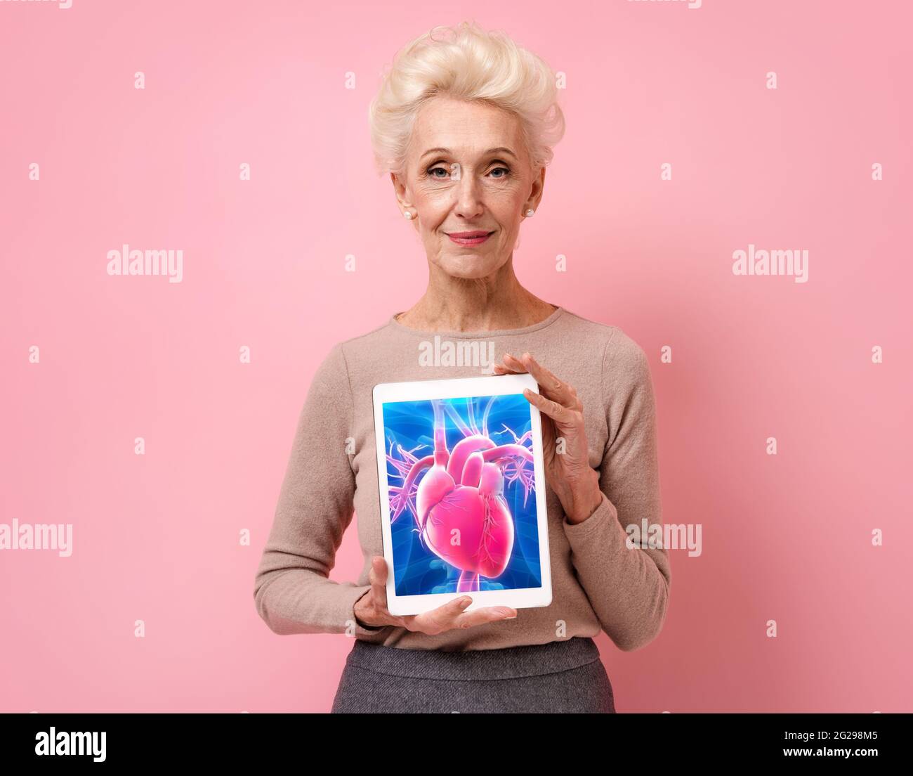 Une femme attirante montre l'image radiologique du cœur. Photo d'une femme âgée souriante avec une tablette dans les mains sur fond rose. Concept médical Banque D'Images