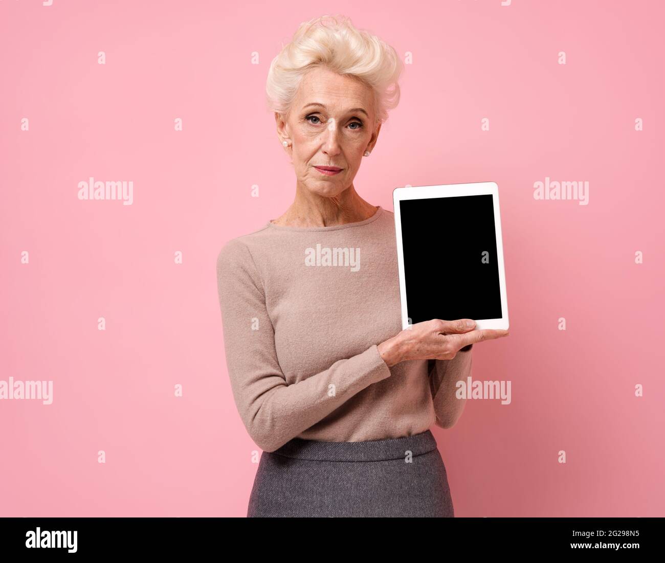 Femme souriante tenant une tablette numérique avec un écran vierge. Photo d'une femme âgée sur fond rose. Banque D'Images