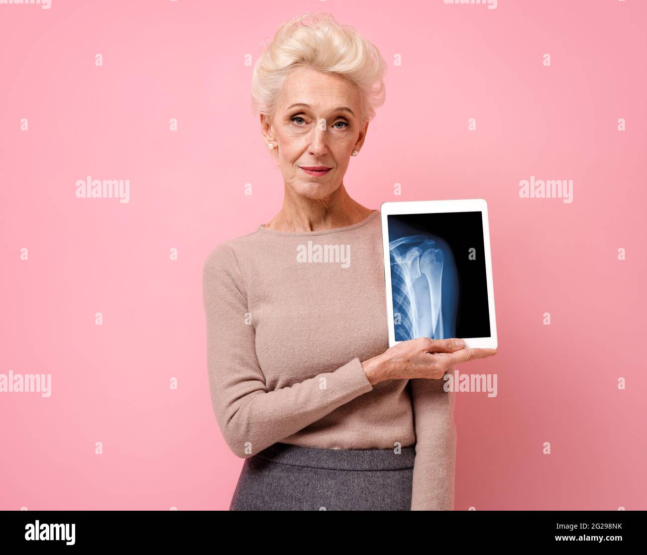 Une femme attirante présente une radiographie de l'articulation de l'épaule. Photo d'une femme âgée souriante avec une tablette dans les mains sur fond rose. Concept médical Banque D'Images